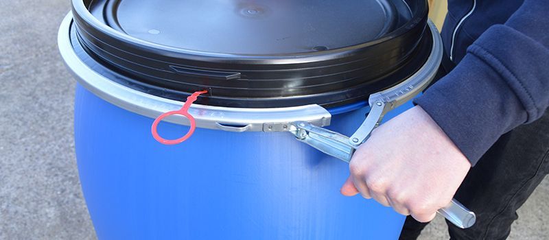 Blue plastic barrel with black lid being opened by hand